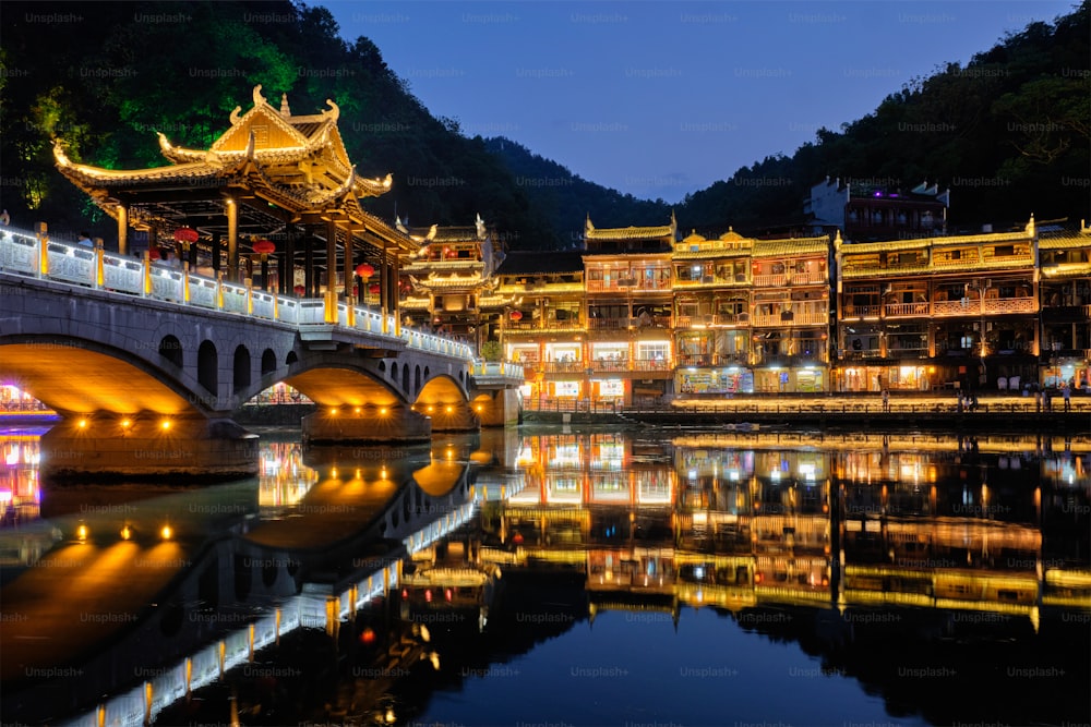 Chinese tourist attraction destination - Feng Huang Ancient Town (Phoenix Ancient Town) on Tuo Jiang River with bridge illuminated at night. Hunan Province, China