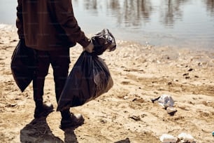 Unrecognizable man standing on the beach and holding bags full of trash he picked up. Copy space.