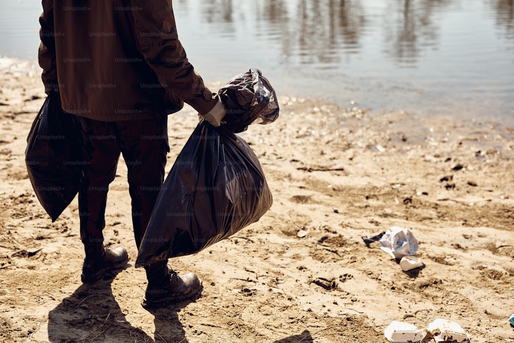 Un hombre irreconocible parado en la playa y sosteniendo bolsas llenas de basura que recogió. Espacio de copia.