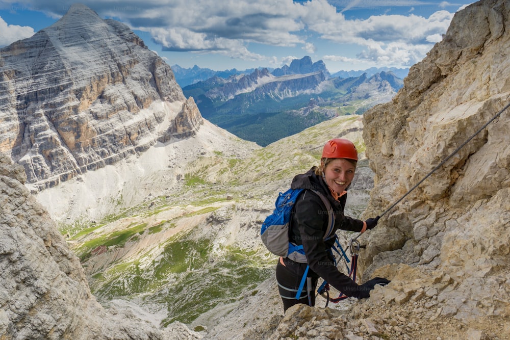 Vista horizontal de una atractiva escaladora en una empinada vía ferrata en los Dolomitas italianos con una gran vista detrás