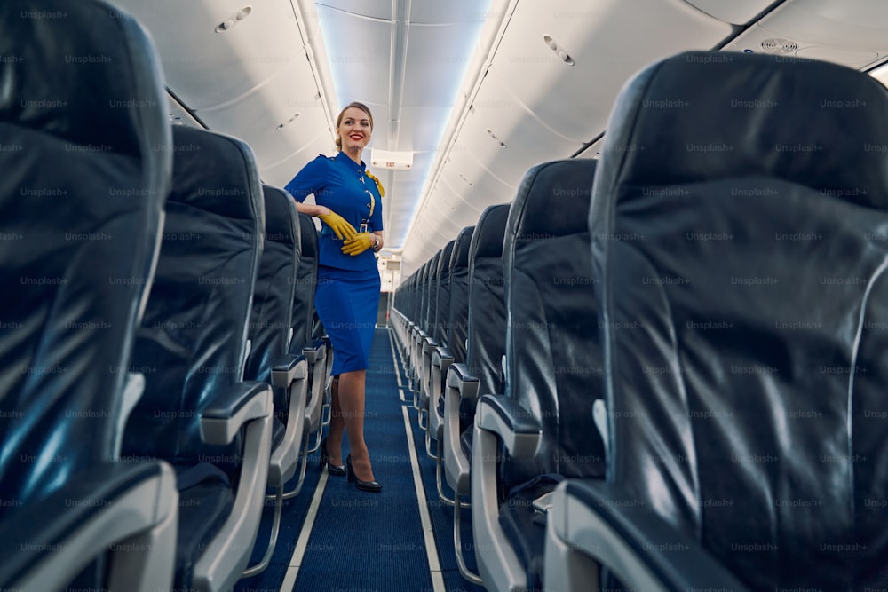Full-sized portrait of a smiling charming young blonde air hostess leaning on the airline seat