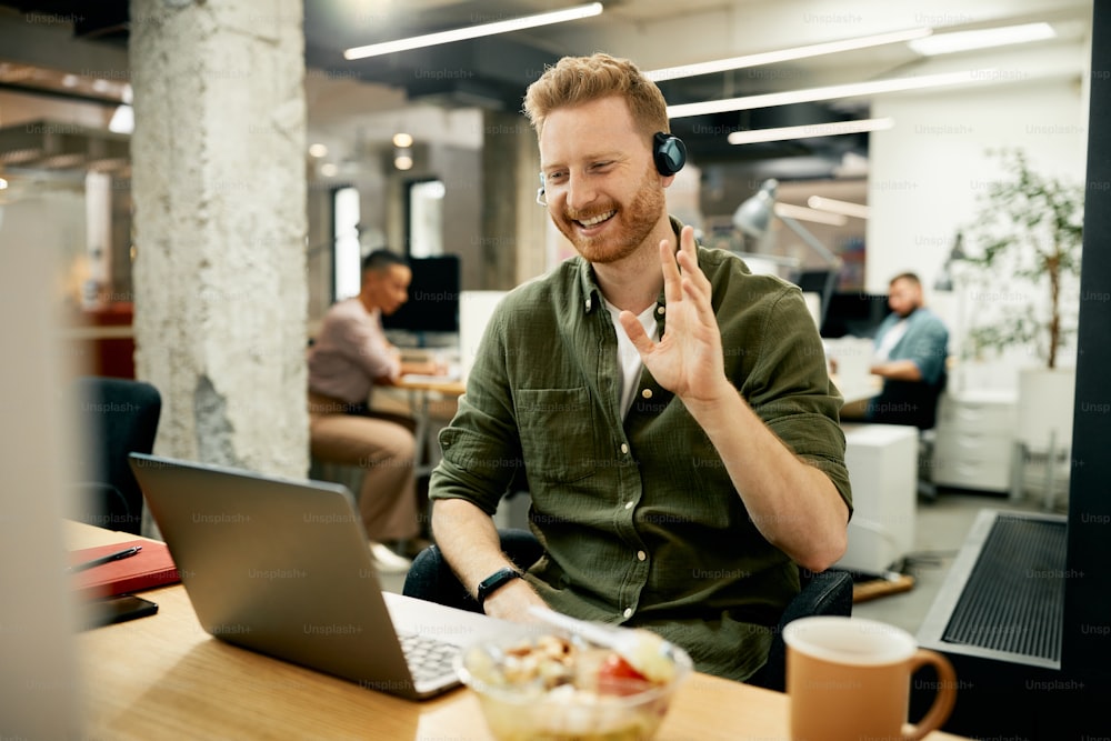 Uomo d'affari felice che usa il computer portatile e saluta qualcuno durante la videochiamata dall'ufficio.