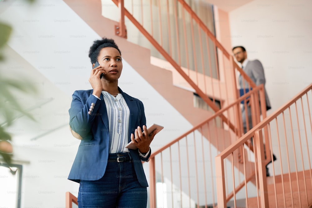 African American businesswoman communicating over mobile phone while standing in a lobby of an office building.