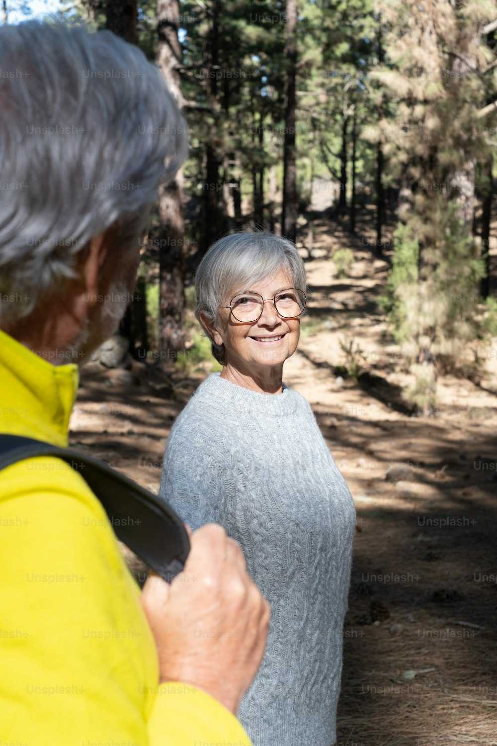 Happy senior couple looking at each other walking in the forest holding hands. Caucasian active elderly gray haired people enjoying vacation freedom and nature hiking in footpath in a sunny day