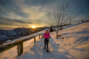 Mujer joven sola en caminata con raquetas de nieve en hermoso día de puesta del sol
