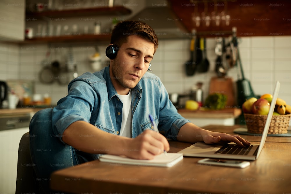 Trabalhador freelancer usando laptop e fazendo anotações enquanto trabalha em casa.