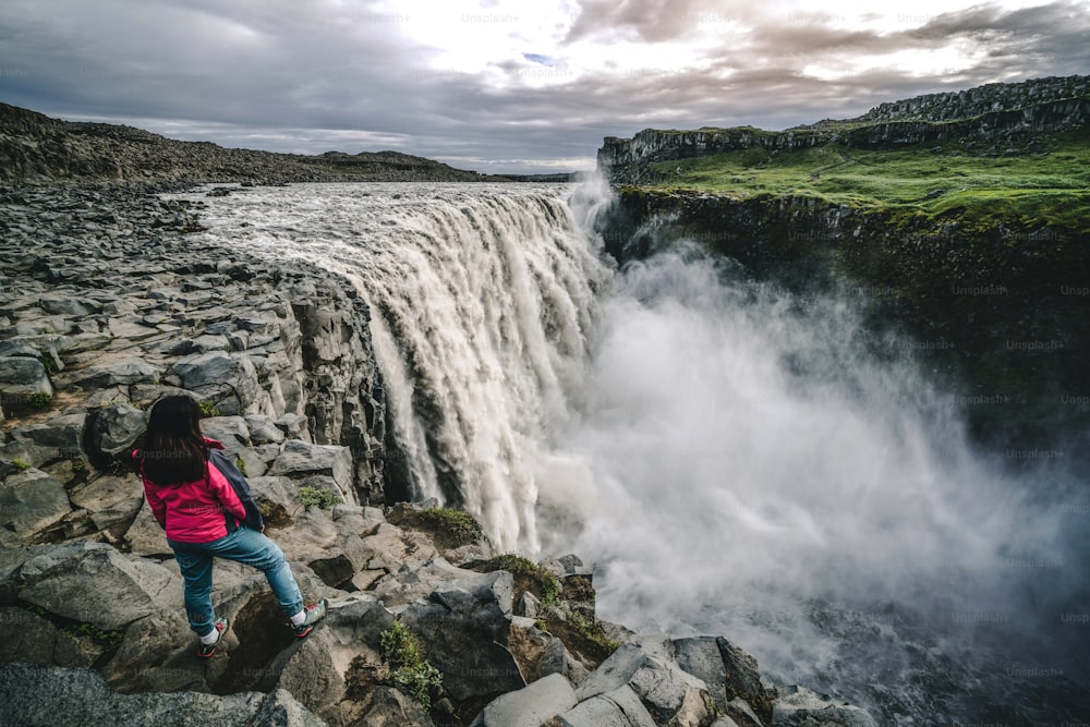 Woman traveler at amazing Iceland landscape of Dettifoss waterfall in Northeast Iceland. Dettifoss is a waterfall in Vatnajokull National Park reputed to be the most powerful waterfall in Europe.