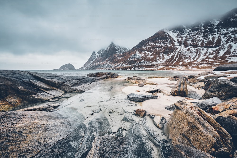 Costa rochosa do fiorde do mar norueguês no inverno com neve. Praia de Haukland, Ilhas Lofoten, Noruega