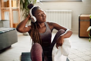Young African American athletic woman enjoying in music over headphones while taking a break during home workout.