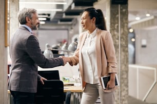 Asian CEO and her male coworker shaking h ands while greeting in the office.