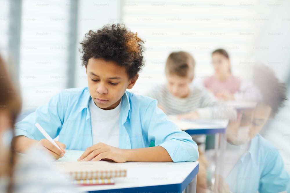 Horizontal medium portrait of pensive African American sitting in classroom working on lesson task, copy space