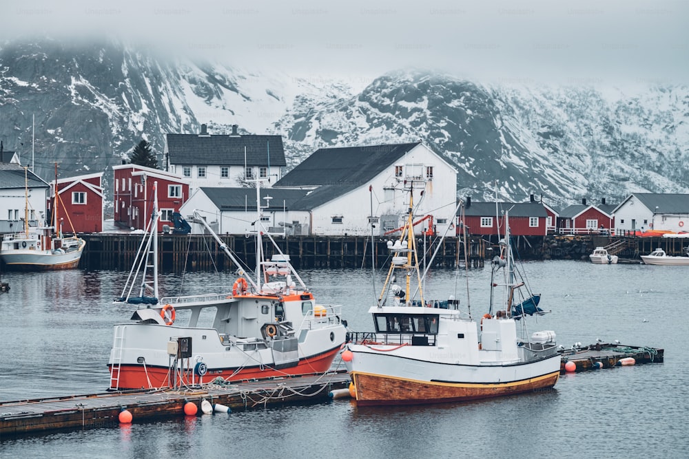Cais com navios na vila de pescadores de Hamnoy nas Ilhas Lofoten, Noruega com casas de rorbu vermelho no inverno