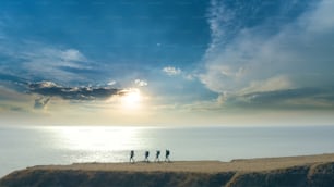 The group of four people walking to the mountain edge near the sea