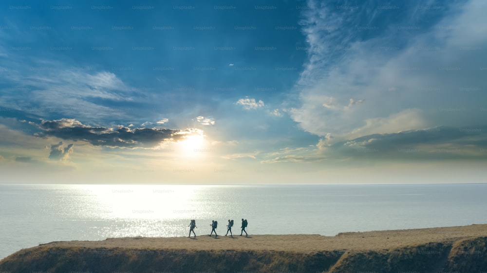 The group of four people walking to the mountain edge near the sea