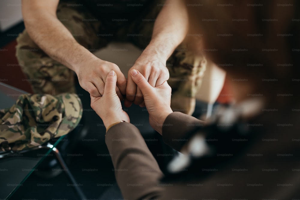 精神保健センターでカウンセリング中にセラピストと手をつないでいる軍人の接写。