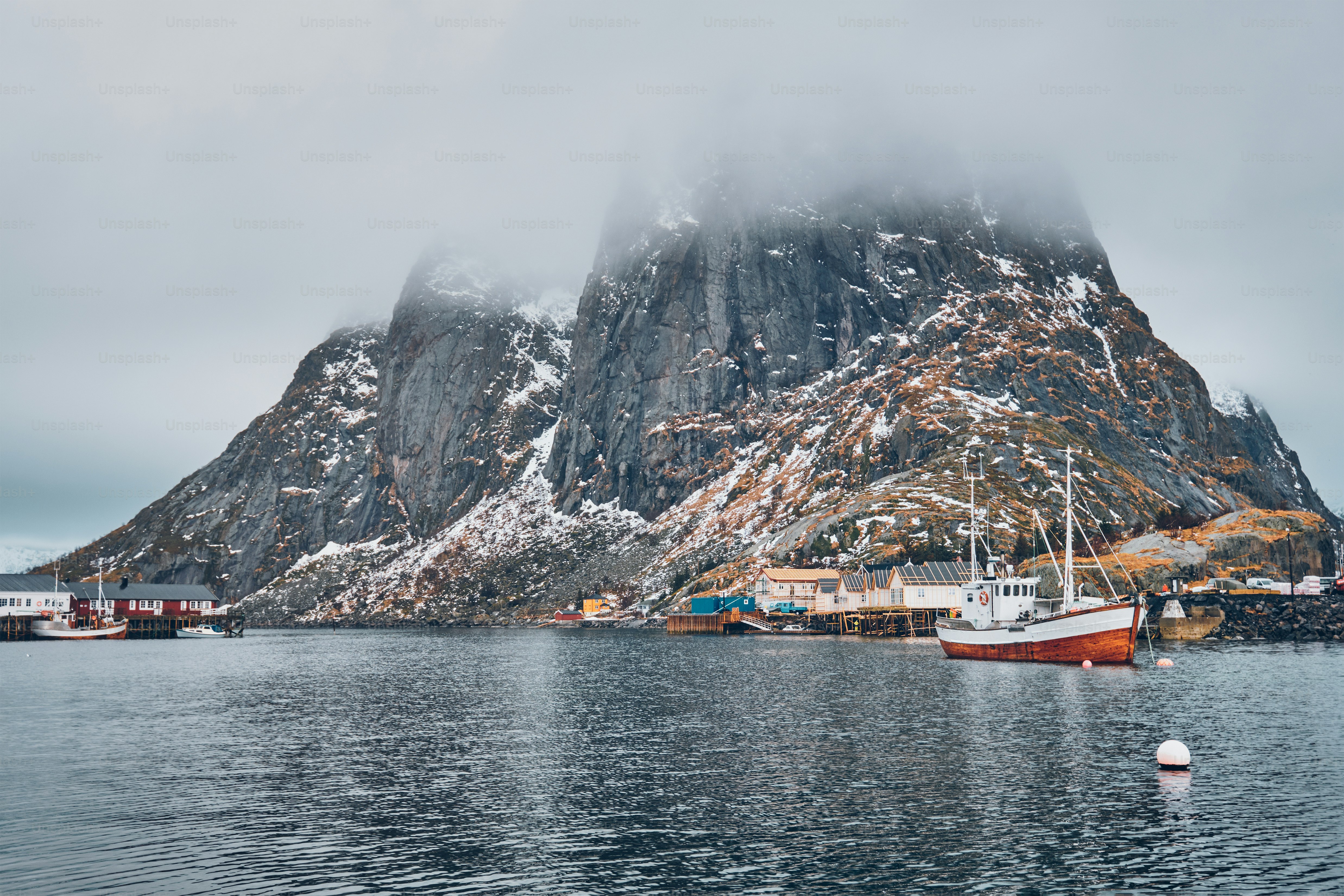 Ship fishing boat in Hamnoy fishing village on Lofoten Islands, Norway with red rorbu houses. With falling snow