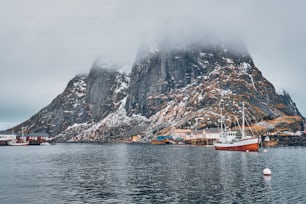 Barca da pesca a nave nel villaggio di pescatori di Hamnoy sulle isole Lofoten, Norvegia con case rorbu rosse. Con la neve che cade