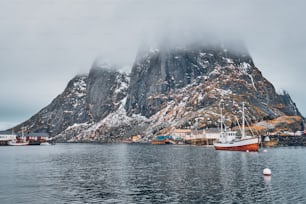 Ship fishing boat in Hamnoy fishing village on Lofoten Islands, Norway with red rorbu houses. With falling snow