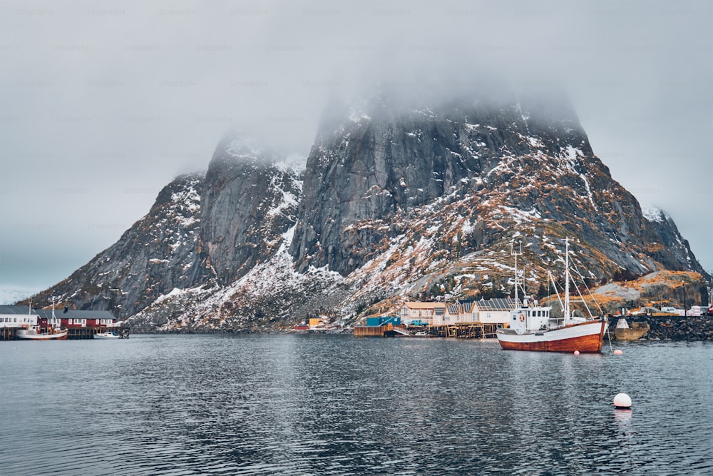 Barca da pesca a nave nel villaggio di pescatori di Hamnoy sulle isole Lofoten, Norvegia con case rorbu rosse. Con la neve che cade