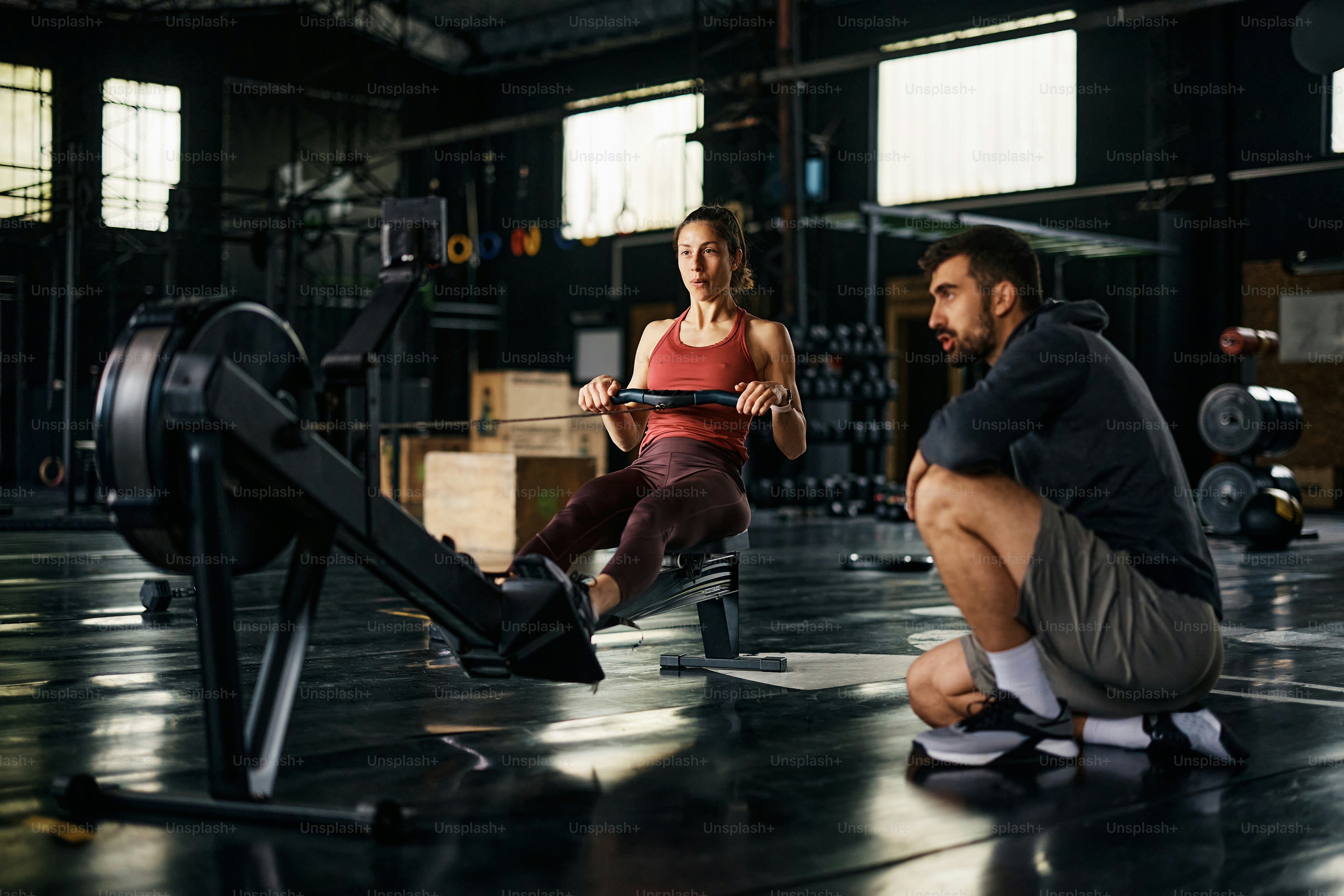 Young sportswoman practicing on rowing machine during sports training with her personal trainer in a gym.
