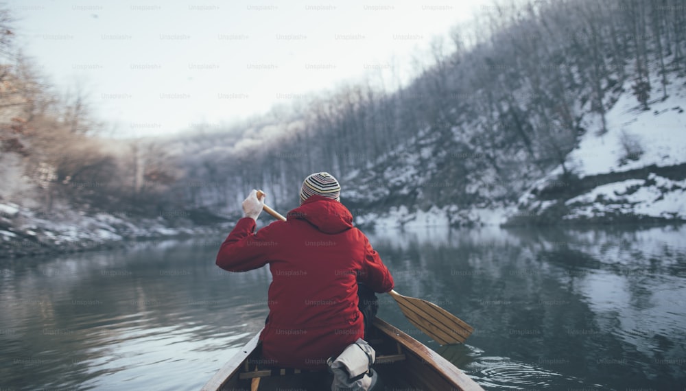 Rear view of man paddling on winter canoe ride.