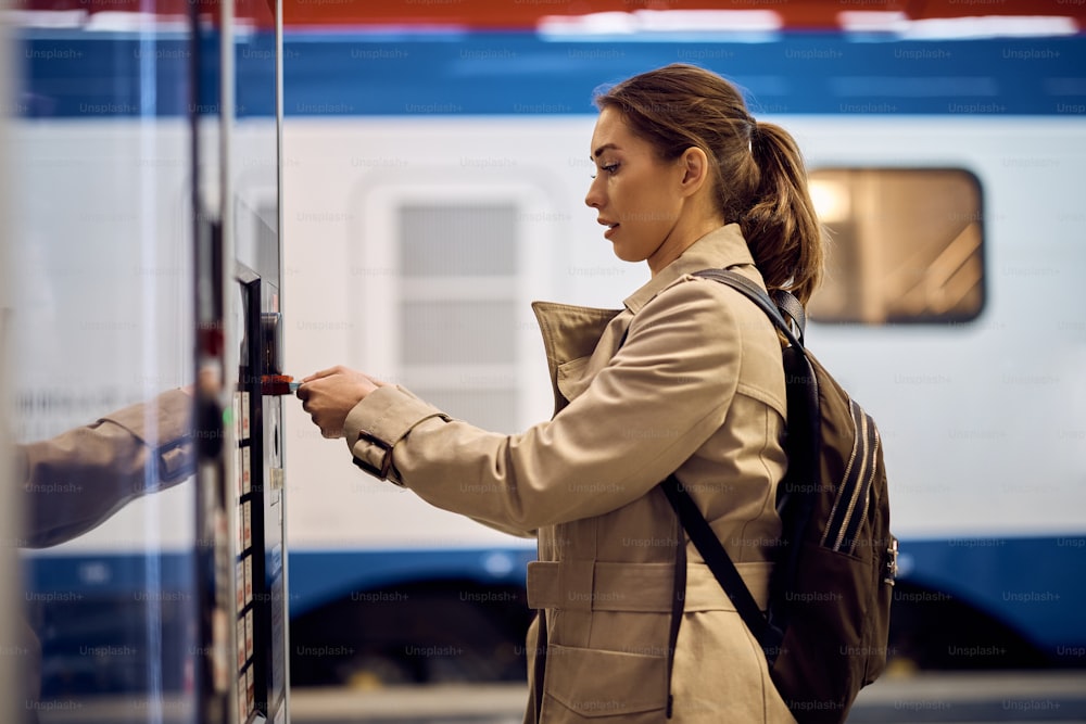 Une passagère achète un billet de train à un distributeur automatique de billets à la gare.