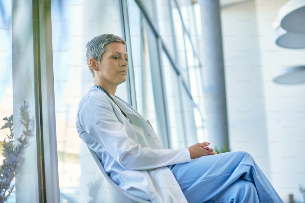 Low angle view of female doctor sitting in hallway and thinking of something in the hospital.