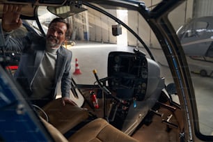 Lächelnder zufriedener, fokussierter, eleganter, reifer kaukasischer Kunde untersucht das offene Cockpit des Hubschraubers