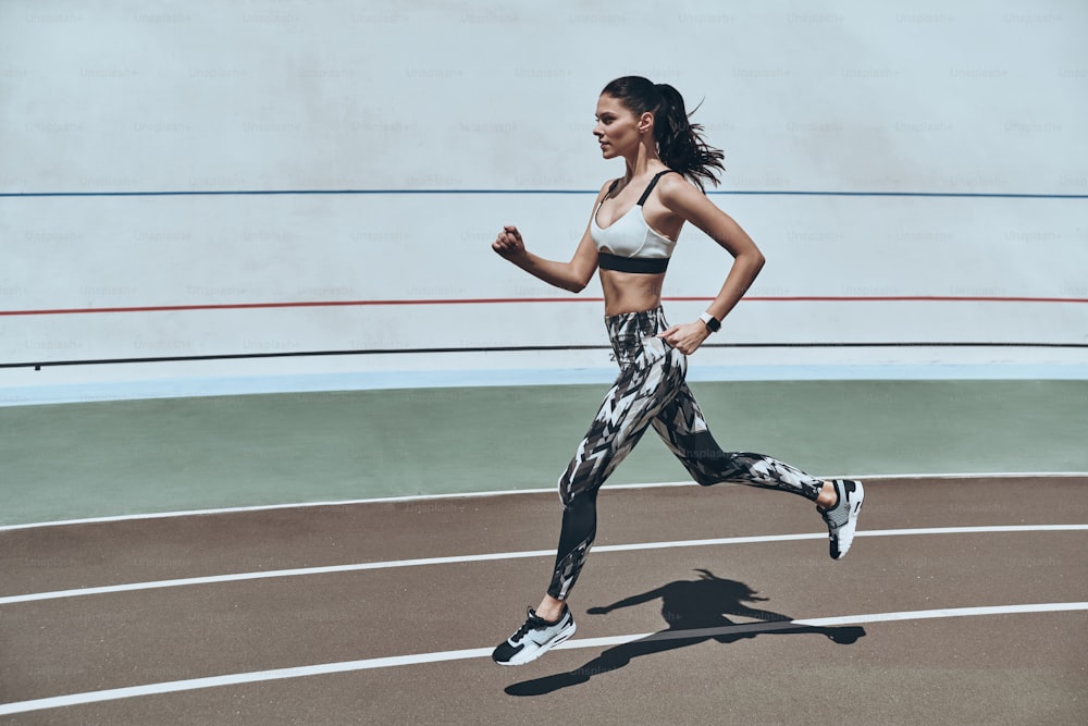 Lunghezza completa di giovane donna in abbigliamento sportivo che fa jogging mentre si esercita all'aperto