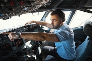 Serious Caucasian man in a cockpit showing something behind the glass before the flight start