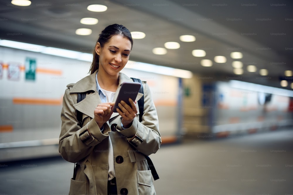 Young happy passenger text messaging on her cell phone at subway station. Copy space.