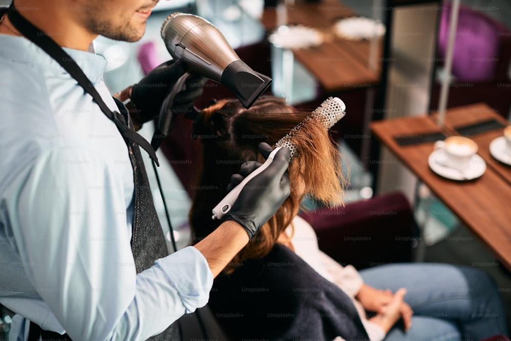 CLose0up de cabeleireiro usando escova redonda enquanto penteia o cabelo da mulher no salão de cabeleireiro.