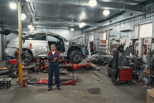 Full length of woman automobile technician standing near car in repair service station