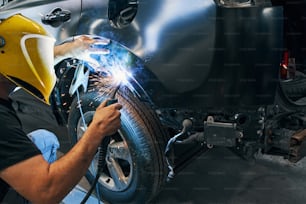 Persona en el taller de reparación de automóviles que suelda la pieza del automóvil por encima de la rueda con la pantalla protectora de la cara en la cara