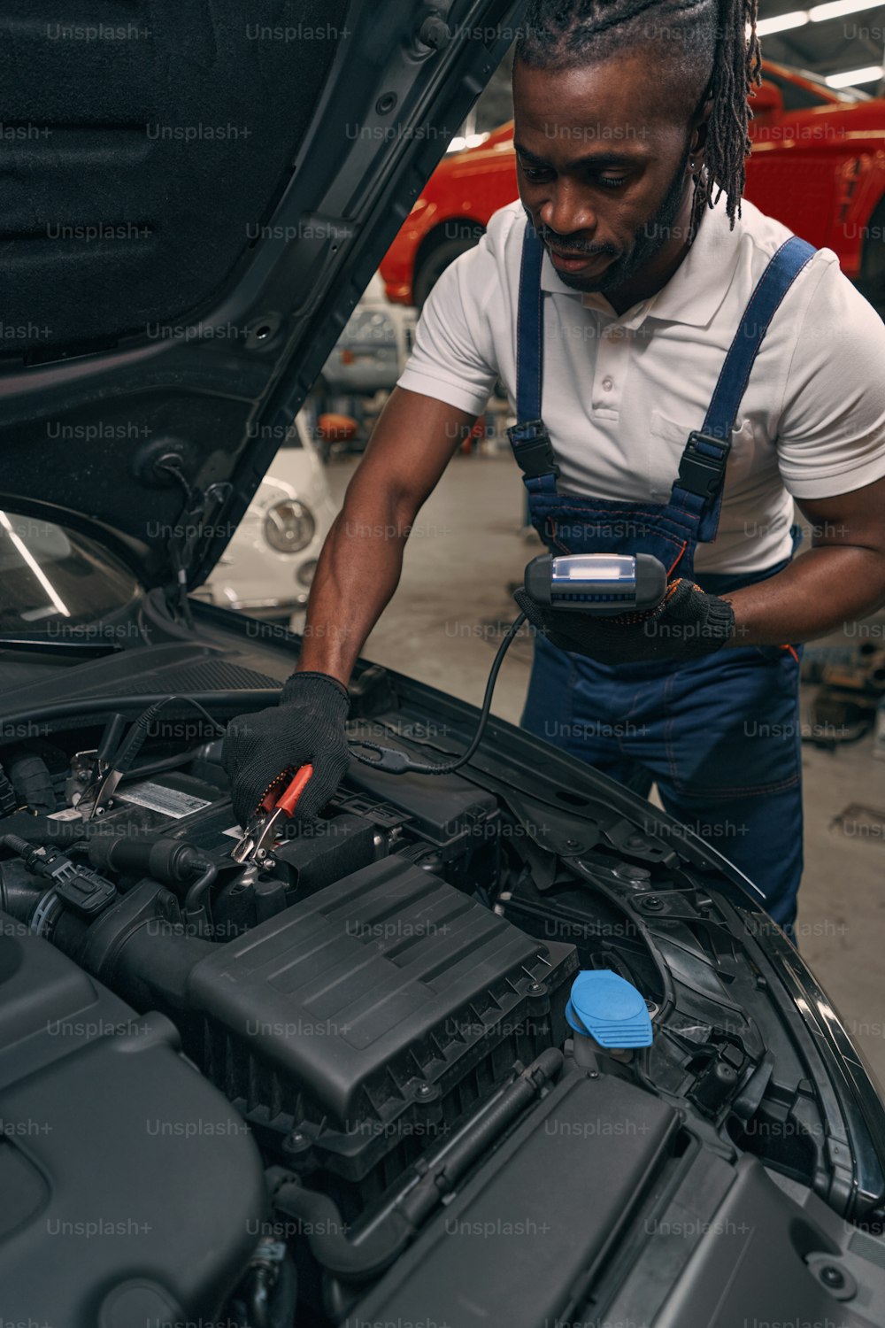 Multiracial repairman testing car battery under hood with automotive battery load tester in auto repair shop