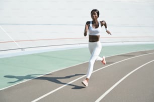 Beautiful young African woman in sports clothing running on track outdoors