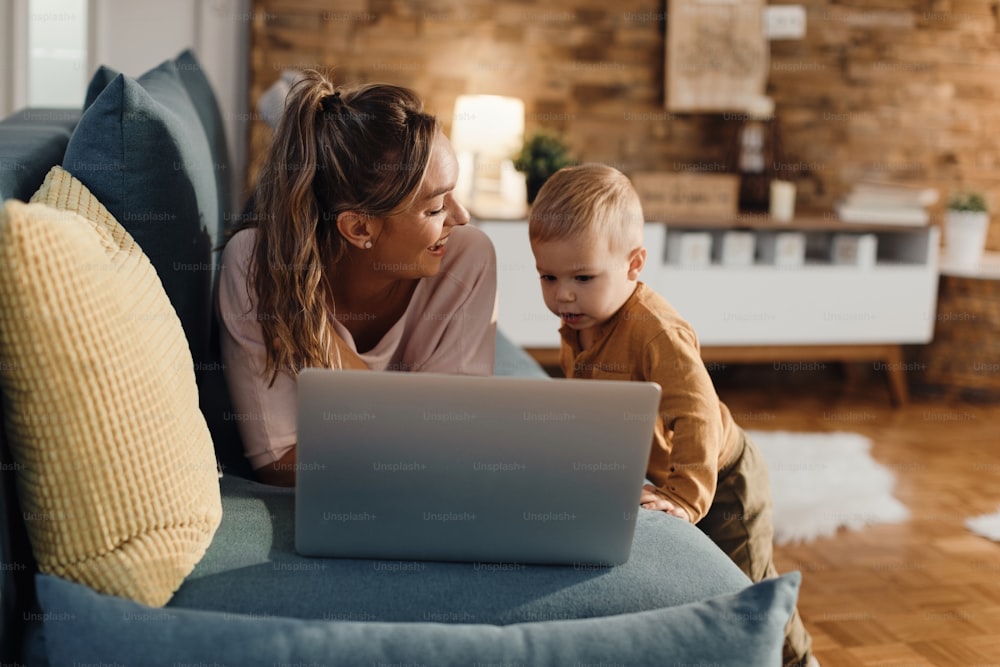 Happy mother using laptop with her small son while lying down on sofa at home.