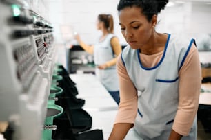 Jeune couturière afro-américaine travaillant à la machine à broder dans une usine de vêtements. n