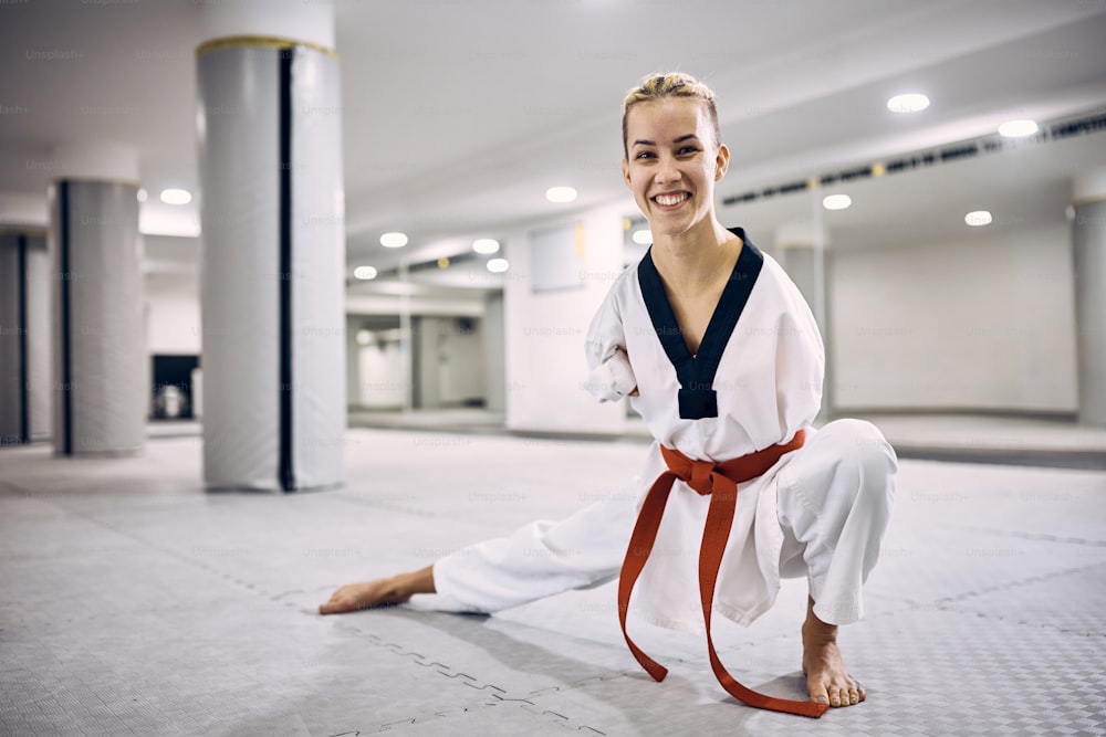 Luchadora de taekwondo motivada con para-habilidad calentando durante el entrenamiento deportivo en el gimnasio y mirando a la cámara.