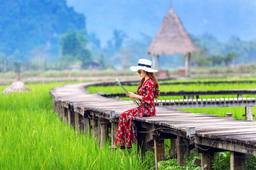 Young woman sitting on wooden path with green rice field in Vang Vieng, Laos.