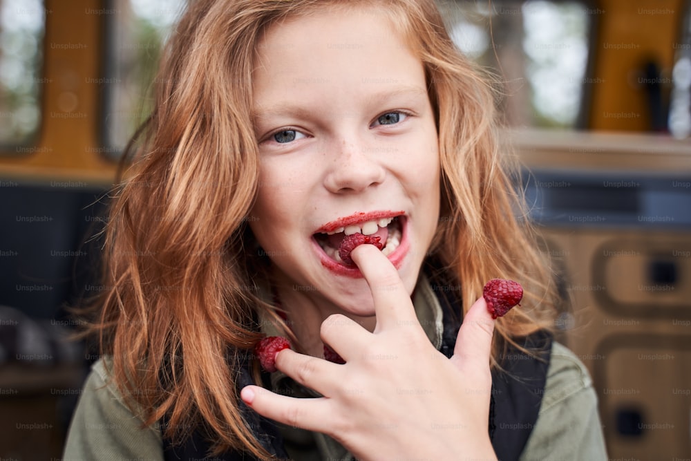Mmm tasty! Coquettish girl tasting ripe and fresh raspberries from her fingers while looking at the camera