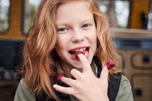 Mmm tasty! Coquettish girl tasting ripe and fresh raspberries from her fingers while looking at the camera