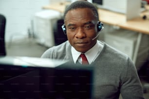 Afroamerikanischer Kundendienstmitarbeiter, der im Büro an einem Desktop-PC arbeitet.