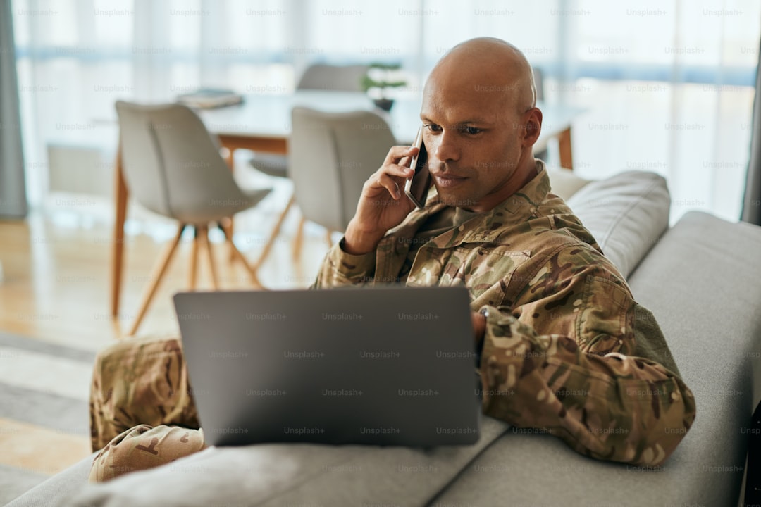African American veteran using laptop while talking on mobile phone in the living room.
