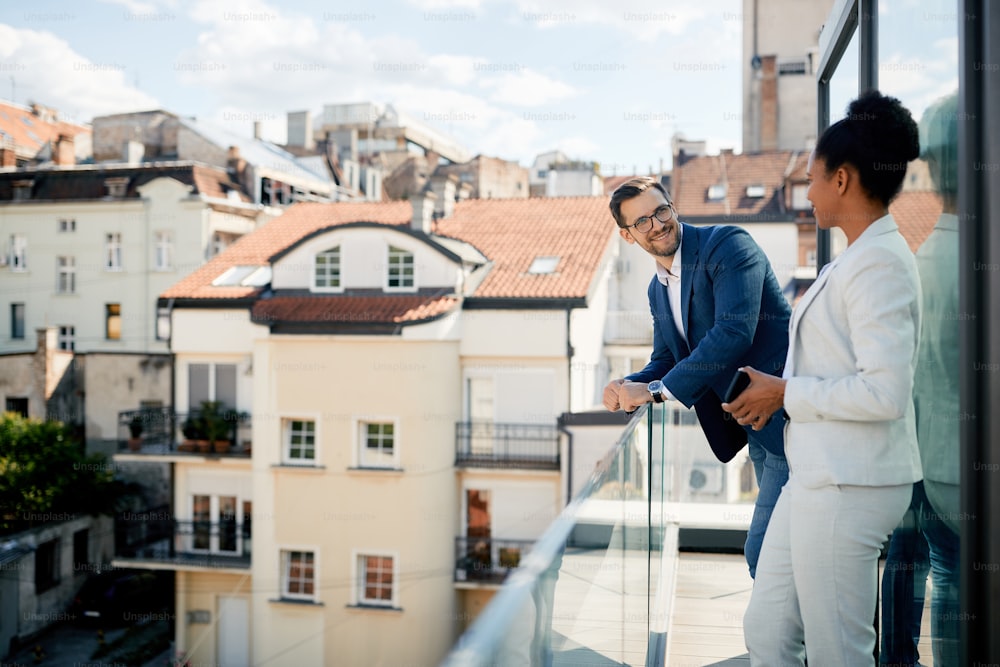 Happy businessman talking to African American colleague during  their break on a balcony.