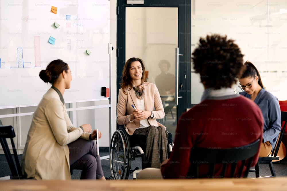 Femme d’affaires heureuse en fauteuil roulant donnant une présentation à ses collègues le bureau.