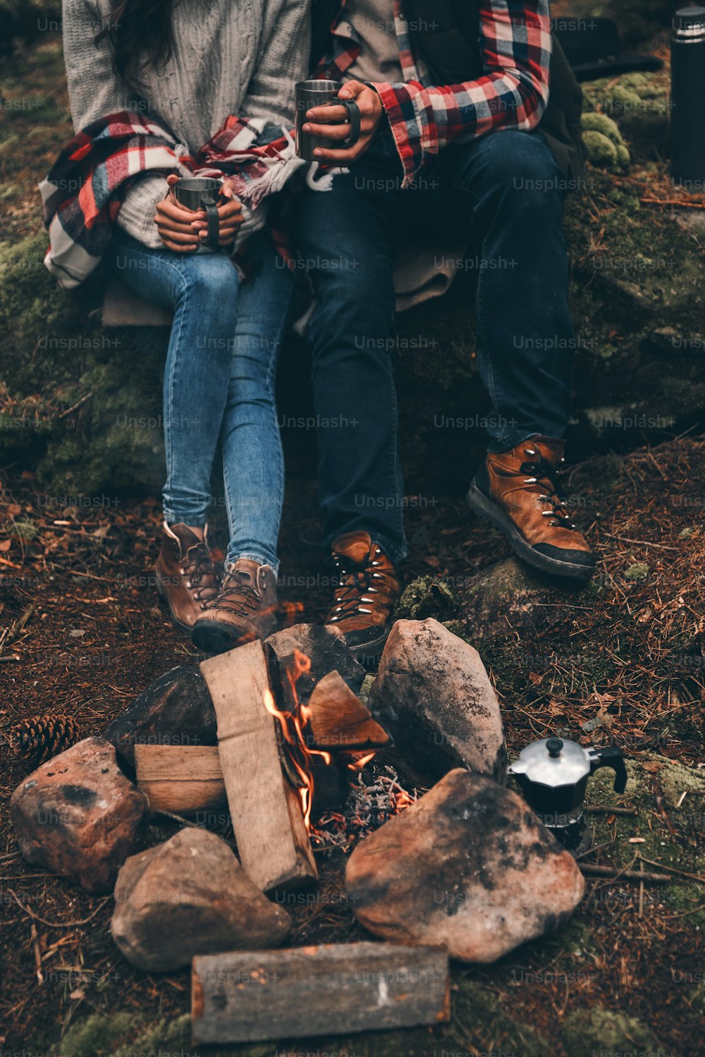 Nahaufnahme eines jungen Paares, das Tassen hält, während es sich am Lagerfeuer aufwärmt