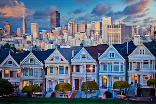 캘리포니아 샌프란시스코의 유명한 페인티드 레이디스(Painted Ladies)가 일몰과 고층 빌딩을 배경으로 빛나고 있습니다.