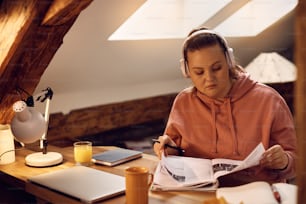 Young woman wearing headphones while studying for upcoming exams at home.