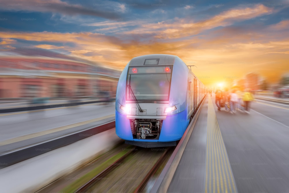 Gare avec train de banlieue rouge à grande vitesse moderne avec effet de flou de mouvement au beau coucher de soleil coloré